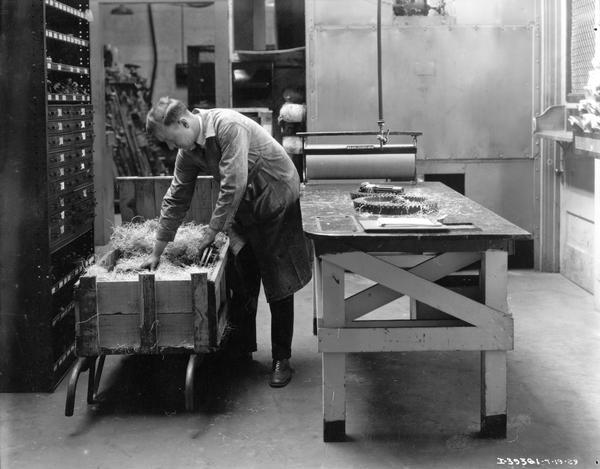 Employee unpacking parts from a straw-lined crate at an International Harvester dealership.