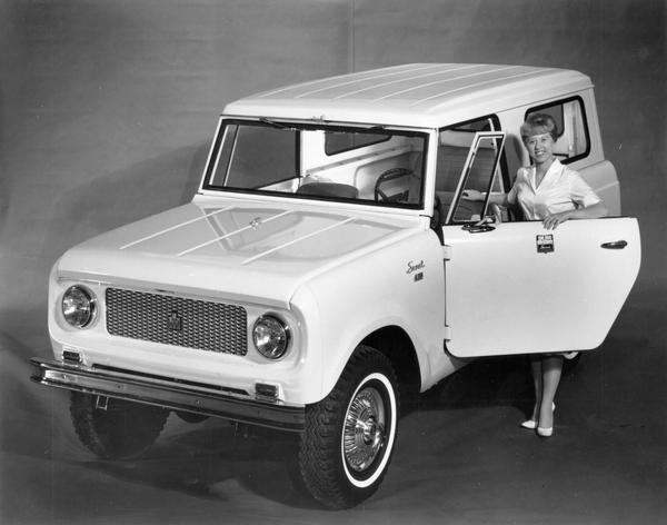 Press release photograph of a model posing with International's Red Carpet Series Scout pickup. Original caption reads: "The Red Carpet Series Scout has been created by International Harvester Company to mark the production of the 100,000th Scout by International since the line's introduction 3 1/2 years ago. Sparkling white finish highlights on interior of high-pile red carpet, red upholstery and red trim."