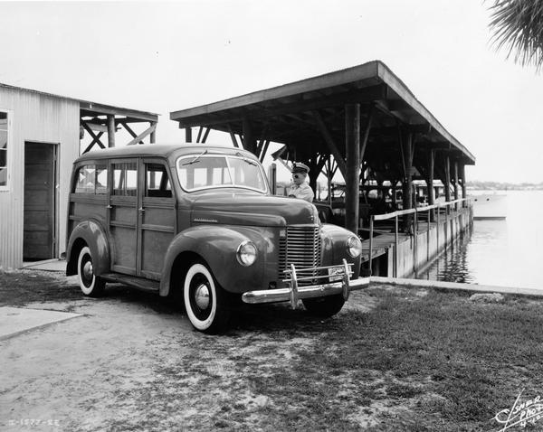 Young man opening the driver's door of an International Model K-1 station wagon ("woody") parked along a dock.