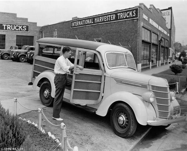 Young man inspecting the interior of an International Model D-2 station wagon ("woody") outside an International Harvester dealership.