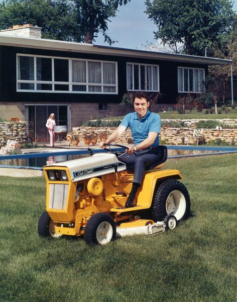 Color advertising photograph of a man mowing a suburban lawn with an International Cub Cadet lawn tractor. In the background a woman is tending to a grill by a pool.