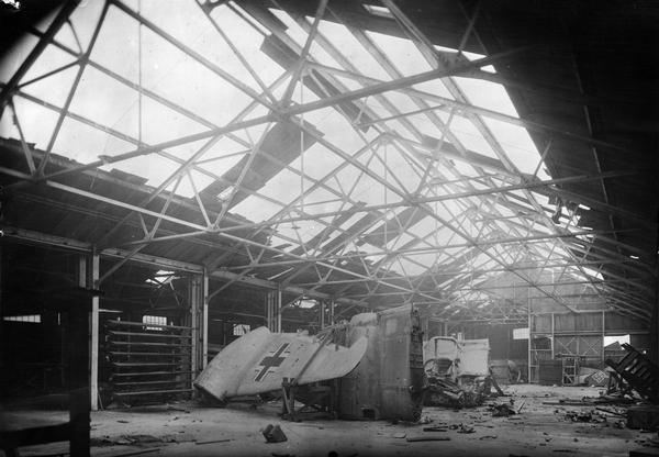Damaged interior of an International Harvester warehouse attached to the company's branch house at Nancy, France. Nazi Luftwaffe aircraft wings and tailfins are visible among the rubble. Total estimate for damage done to warehouse was 1,450,187.50 francs. Original report reads: "The property was occupied by German armed forces. Before leaving Nancy they blew up the airplanes which they had sheltered in the warehouse at the same time damaging the roof, sides, etc., of the building."