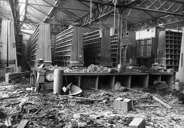 Damaged interior of International Harvester's branch house at Nancy, France. Rubble is strewn across the floor around rows of parts bins.  Original report reads: "The premises were hit by a shell during the hostilities and suffered damage."