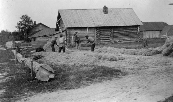 Four men threshing grain by hand while two children are watching. The location is Russia, probably near Lubertzy.
