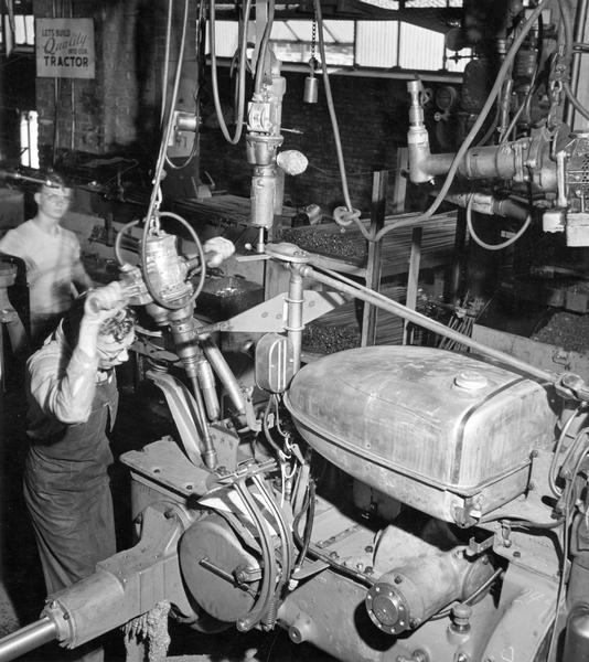 Factory worker tightening bolts on a Farmall tractor on the assembly line at International Harvester's Farmall Works.