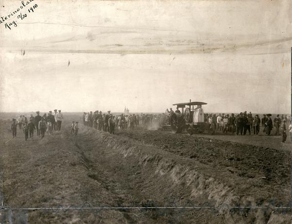 Crowd of men, women and children gathered at Ekaterinburg (Ekaterinoslav) to witness a demonstration of the first International Harvester tractor shipped to Russia. The tractor is pulling a breaking plow.