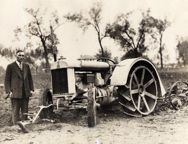 Farmer and mechanic F.L. Zybach, 32, standing beside his invention -- a Fordson tractor with a front-mounted plow equipped for "driverless operation." Original caption reads: "A farmer for some time, he tired of sitting behind a plow and hit upon a scheme of a plow that would turn over a field without the touch of a hand. All that he does is guide the plow in the first furrow, on the outside of the field, rounding off the corners. From then on the machine runs itself until the entire field is plowed. A four foot piece of iron pipe, one end fastened to the front axle, the other end fastened to a curved piece of sheet iron that hugs the furrow wall. The instant the machine tries to stray out of its path, the curved piece of iron releases a spring that shuts off the ignition. The spring can be seen on front axle. All that Zybach does is to sit in the shade of a tree and watch his invention plow his fields."