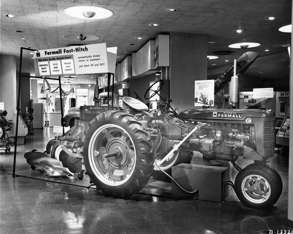 Exhibit in the showroom of International Harvester's General Office building demonstrating the features of the Farmall Fast-Hitch. The exhibit includes a Farmall Super C tractor and what appears to be an automated moving display of the Fast-Hitch mechanism.