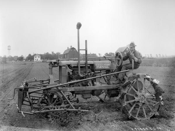 Man operating an early Farmall Regular tractor with attached harrow.