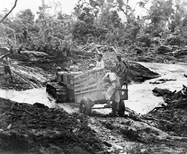 Marines ride through a creek on a trailer pulled by an International crawler tractor (TracTracTor).
