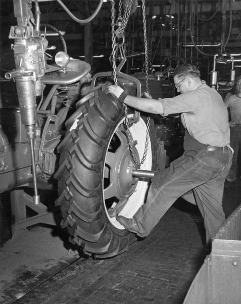 Factory worker installing a wheel on a tractor on the assembly line at International Harvester's Farmall Works.