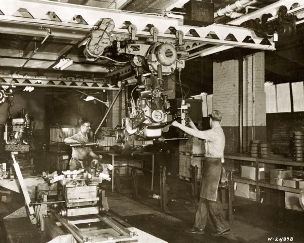Factory workers working on a tractor chassis and engine on an assembly line at International Harvester's Farmall Works.