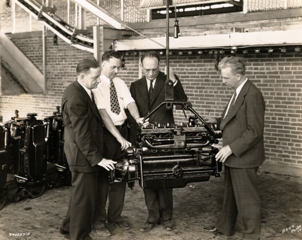 Four men examining a tractor engine at International Harvester's Farmall Works (factory). Original caption reads: "First six cylinder tractor engine at Farmall Works."