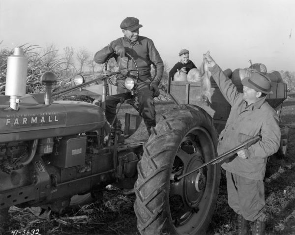 Hunter shows a dead rabbit to a man on a Farmall H tractor and a boy in a wagon full of pumpkins. The caption reads: "Mr. [William] Foreman is on the tractor, Junior Scott of Fithian is in the wagon, and Mr. Vinson E. Gritten is proudly holding the rabbit."