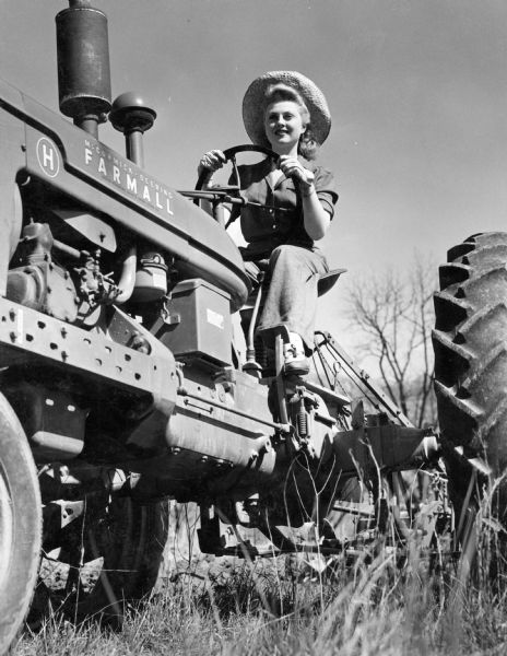 Young woman operating a Farmall H tractor.