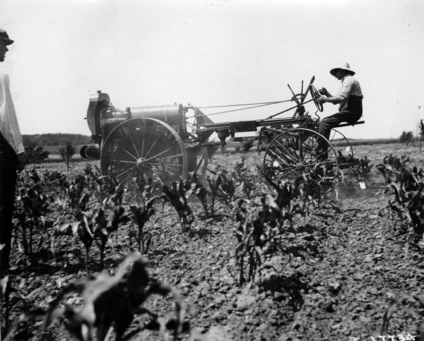 Man operating a Moline Universal tractor. Another man is standing in the left foreground.