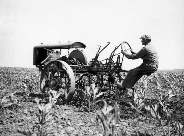 Man operating a Rockford(?) tractor with attached cultivator. The original caption reads:  "Another competitive tractor, probably the Rockford. This tractor was offered to the International Harvester Co., and C.O. Aspenwall was assigned to investigate and report on it. He reported unfavorably.  1918."