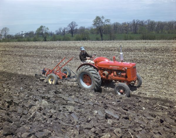 Slightly elevated view of a man in a field operating a McCormick standard W-4 tractor with a plow.