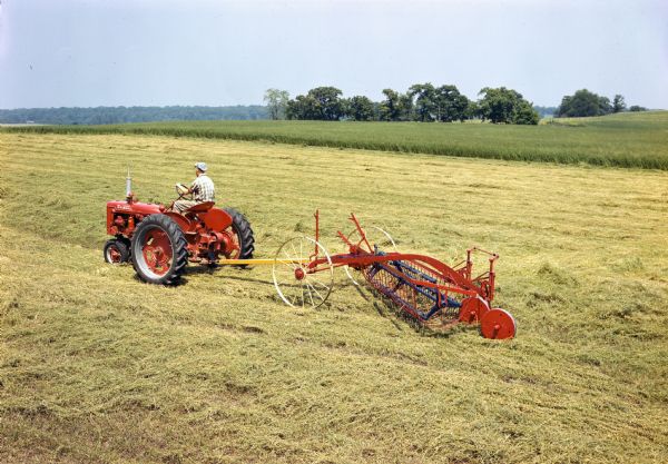 Elevated view of a farmer in a field pulling a hay rake with a McCormick Farmall C tractor.
