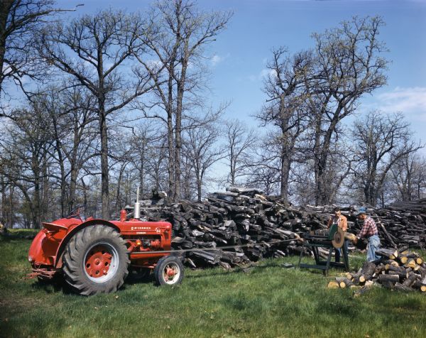 View towards two men cutting wood with a saw powered by a McCormick standard W-4 tractor.