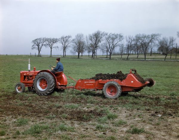 Left side view of a farmer in a field pulling a No. 200 manure spreader with a McCormick standard W-4 tractor.