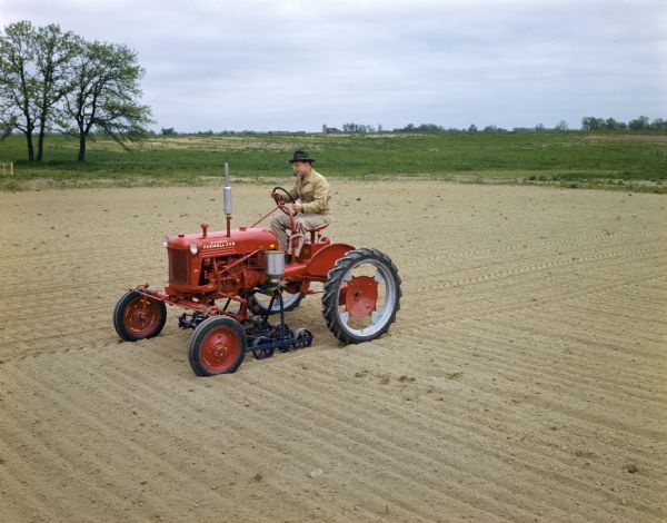 Left side view of a farmer operating a McCormick Farmall Cub tractor over a patch of sand.
