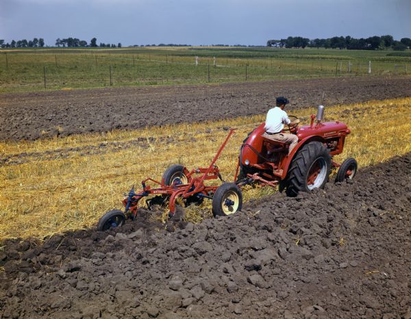 Slightly elevated rear view of a man operating a McCormick standard W-4 tractor and plow in a field.