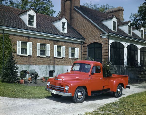 View towards a gardener planting ornamental trees in front of a house. The trees were transported in an International L-120 truck.