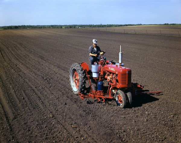 Slightly elevated view of a farmer in a field operating a McCormick Farmall C tractor with a mounted C-220 checkrow planter.