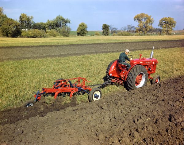 Right side view of a farmer in a field operating a McCormick standard diesel WD-6 tractor with plow.