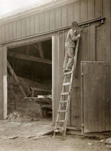 R.A. Hayne on a ladder repairing a barn door.