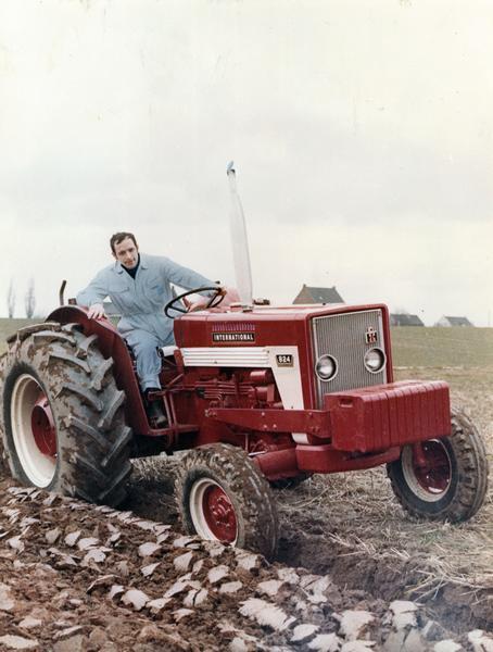 View towards a man plowing a field with an International 824 tractor in Germany. The picture commemorates the launch of the 824 tractor at Neuss Works in Emsland, Germany. The driver is Mr. Gerd Diessel, a graduate engineer in the Neuss Works construction department. The picture appeared as the title page for a 1971 brochure (number GER 54-Z).