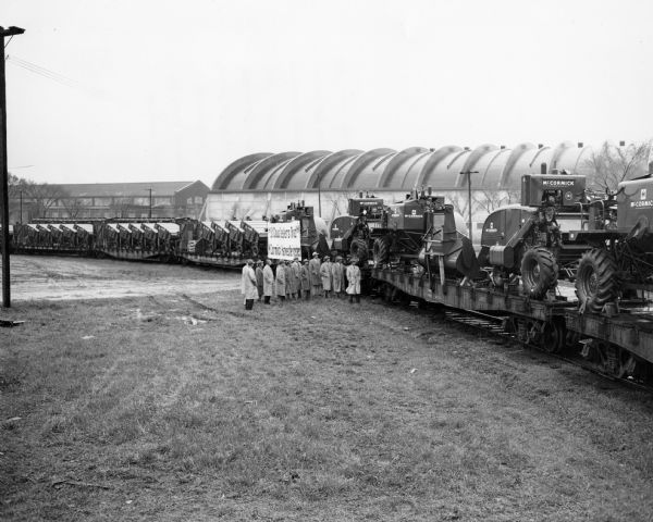 Original caption reads: "The St. Cloud district sales organization looks over the 29-car trainload of McCormick harvester-threshers bound for 47 dealers who participated in this spring sales campaign. In the 29-car train were four cars of No. 141s, three 'mixed' cars of No. 141s and No. 64s, and 22 cars of No. 64s - 105 No. 64s and 11 No. 141s, for a total of 116 combines. Four different railroads participated, after the 29-car train was split up for distribution to dealers. They were the Great Northern, Northern Pacific, Milwaukee and the Soo Line. The train was about 1/3 of a mile long."