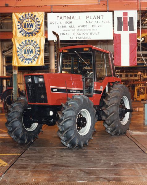 Color photograph of an International 5488 tractor on display in International Harvester's Farmall Works (factory). A sign above the tractor reads: "Final Tractor Built at Farmall." Banners for UAW union locals 1309 & 1310 are hanging near the sign on the left.