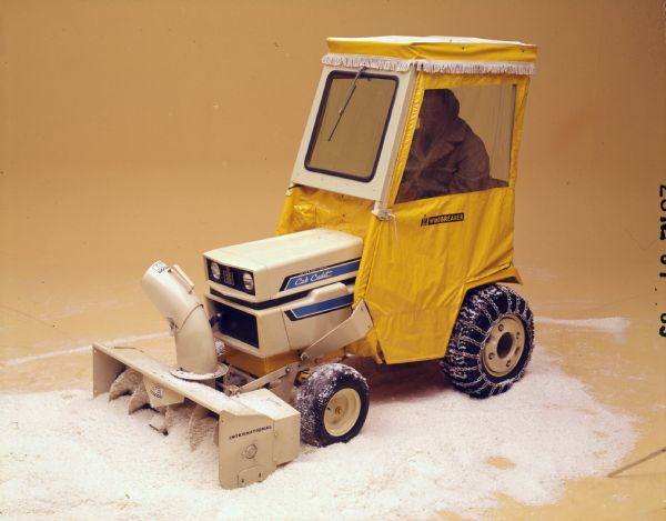 Color advertising photograph of a man operating a 1450 Cub Cadet lawn tractor with snowblower attachment in a studio with fake snow.