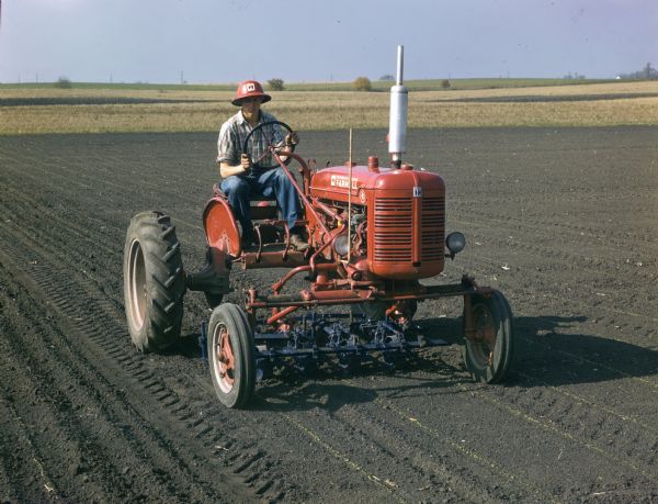 View towards a man operating a Farmall Super A in a field.