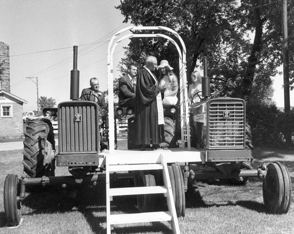 Marriage ceremony on an altar placed between two tractors. Original caption reads: "The American farmer's pride in his profession and his inventiveness was exemplified at the wedding of Gregory Nerroth and his bride, Barbara, of Antioch, Illinois. On an 'altar' erected between two Farmall tractors, Gregory, who operates a 300-acre farm, promised to love, honor... and keep plowing."