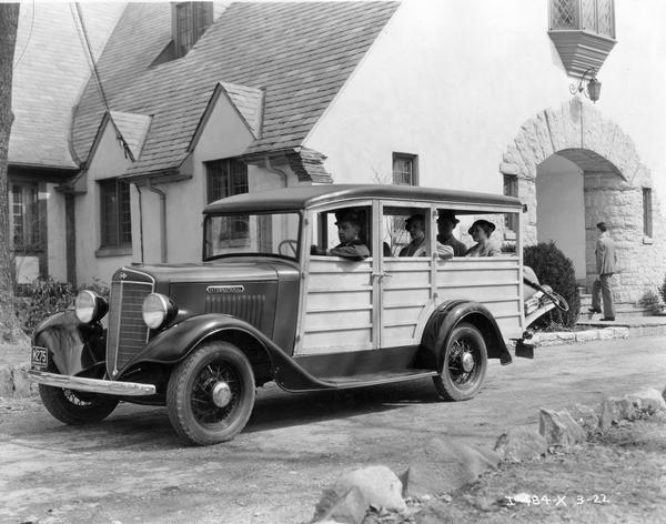 Passengers and luggage in an International station wagon ("woody") outside a large house or hotel.