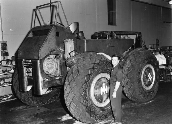Man standing next to an experimental four wheel rubber tire tractor inside an International Harvester engineering(?) facility.