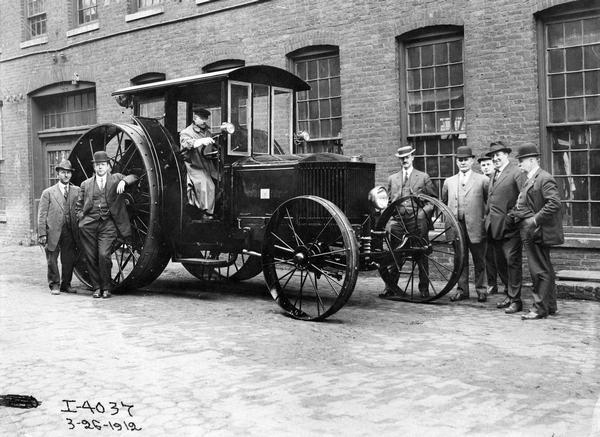 Group of men standing with an experimental tractor outside International Harvester's Deering Works (factory). The original caption reads: "An early design of tractor at Deering Works built and never used."