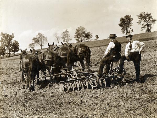Charley Sharpe and Fred Jones working with a disk harrow in a field.  The disk harrow is pulled by four horses. Original caption reads: "Charley Sharpe and Fred Jones trying out a new Disk Harrow for New Zealand at Auburn Works, Auburn, N.Y."
