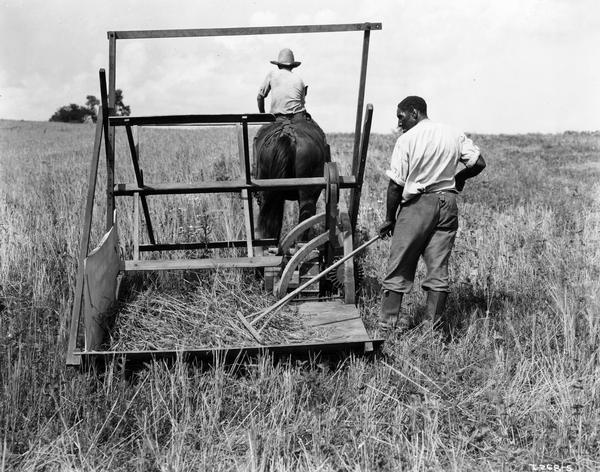 Re-enactors demonstrating a replica of the first reaper built by Cyrus Hall McCormick in 1831. The man raking at the back of the reaper appears to be playing the part of Cyrus McCormick's slave, Jo Anderson. The actor also appeared in the feature film "Romance of the Reaper". The film was produced in 1929 by International Harvester to celebrate the one-hundred year anniversary of the invention of the reaper (also known as the "reaper centennial"). Original caption reads: "Replica of 1831 McCormick Reaper at work at Walnut Grove Farm Rockbridge County Virginia in 1929."