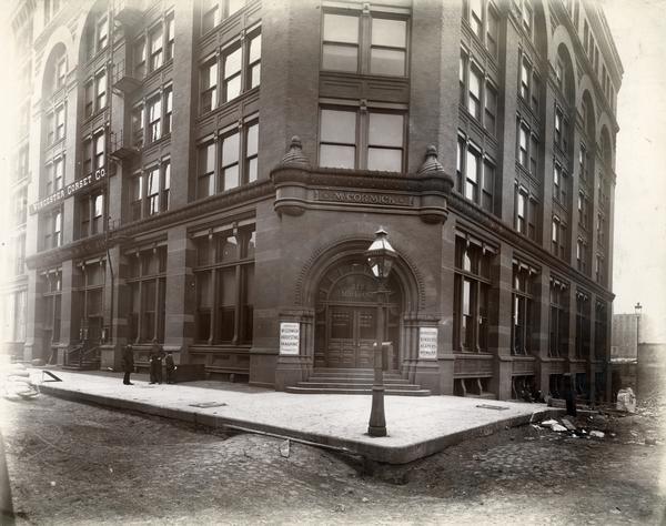 Office of the McCormick Harvesting Machine Company at 212 Market St.  Two men and a boy are standing outside the office building on left side, while three men are sitting at the base of the building on the right. This building served as the McCormick Company's general office from 1885 to 1891. A sign on the second-story on the far left reads: "Worcester Corset Co."