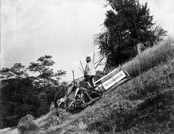 Man operating a horse-drawn McCormick grain binder on the side of a hill.