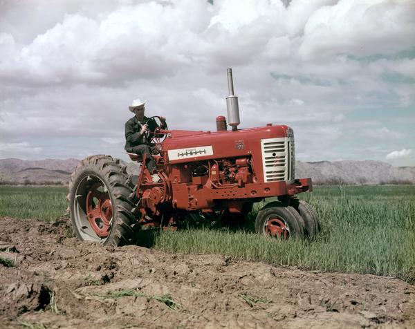 View of a man plowing a field with a McCormick Farmall 450 diesel tractor. Mountains are in the far background.