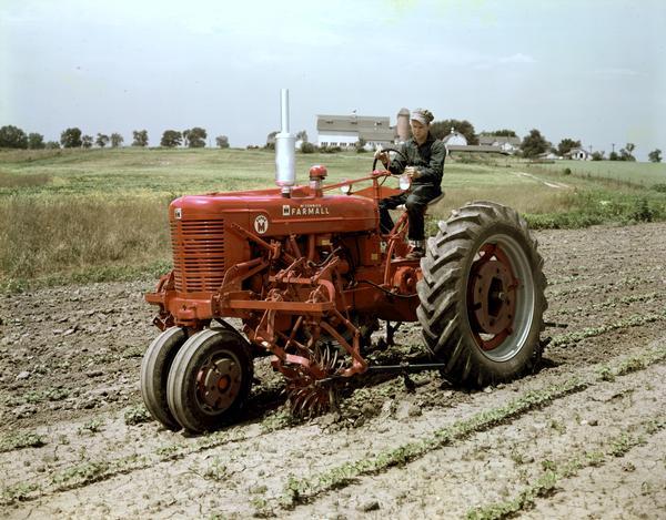 Color photograph of a man operating a McCormick Farmall Super M with rotary cultivator.