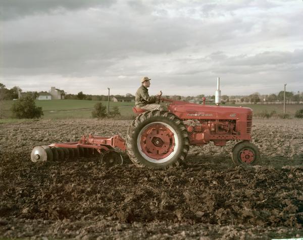 Color photograph of a man plowing a field with a McCormick Farmall 400 tractor and attached disk plow.