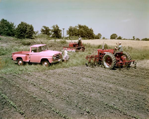 Color photograph of two men and a woman in a field with a pink pickup truck, a crawler tractor (TracTracTor) and a Farmall tractor.