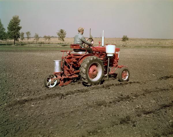 View towards a man operating a Farmall 140 tractor with attached planter in a field.