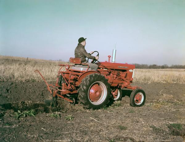 View towards a man plowing a field with a Farmall 140 tractor.